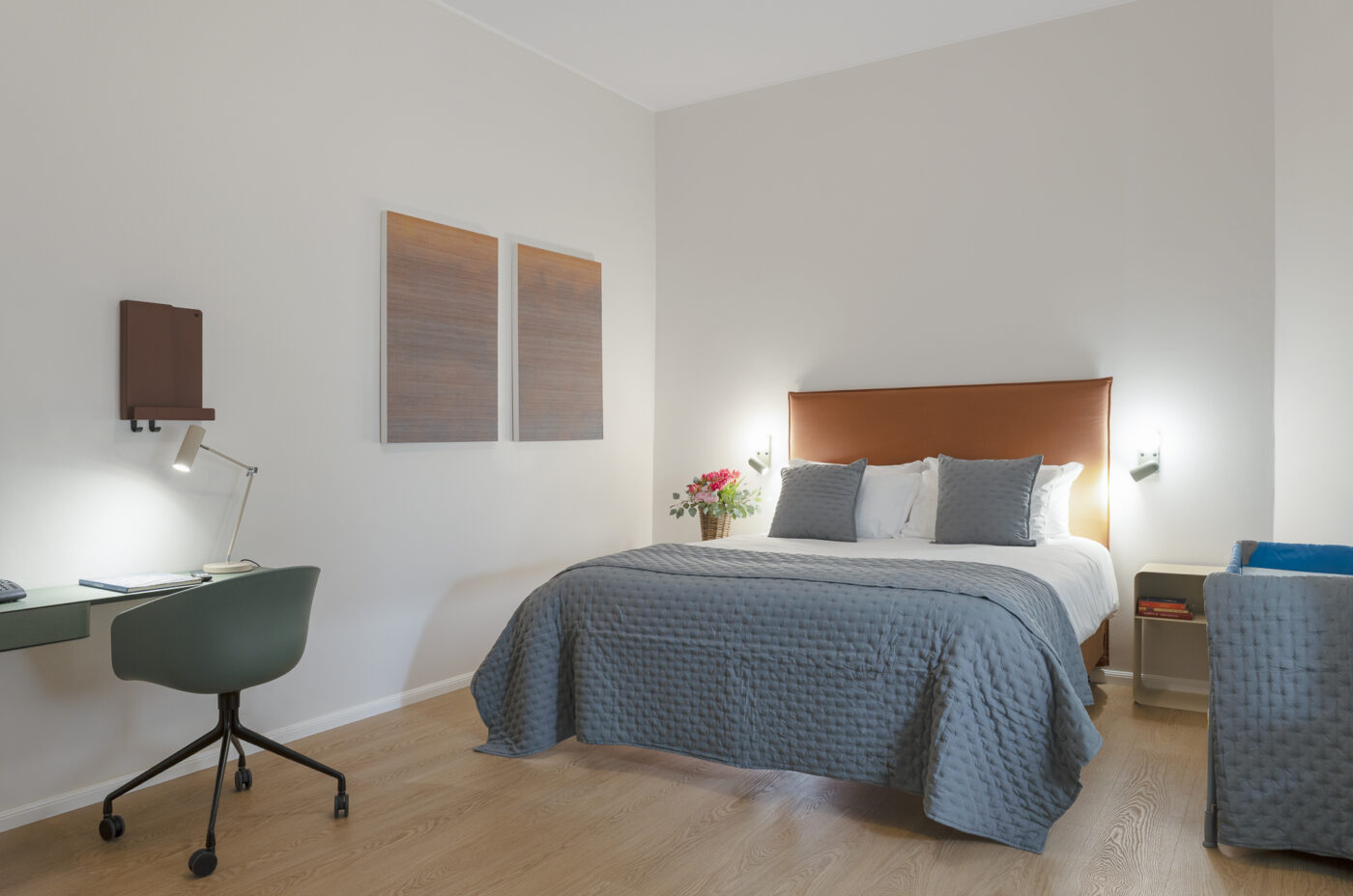 Keyinn Serviced Residences Belair bedroom with blue bedding, a brown headboard, and a desk with a green chair. The space features floral accents and a bright, modern design.