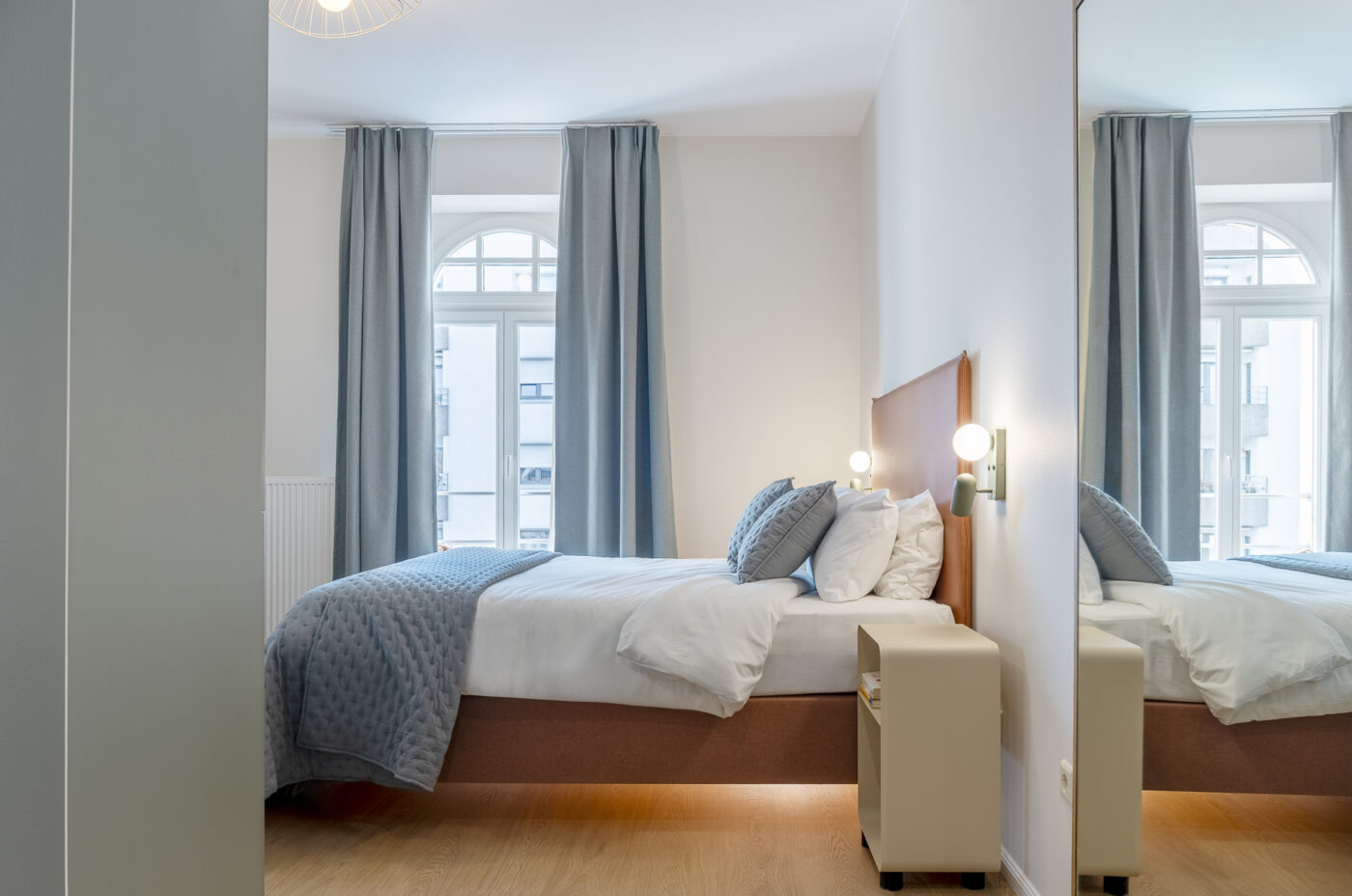 Keyinn Serviced Residences Belair bedroom with a bed, pillows, and arched windows. The space includes curtains, wall art, a lamp, and a mirror.