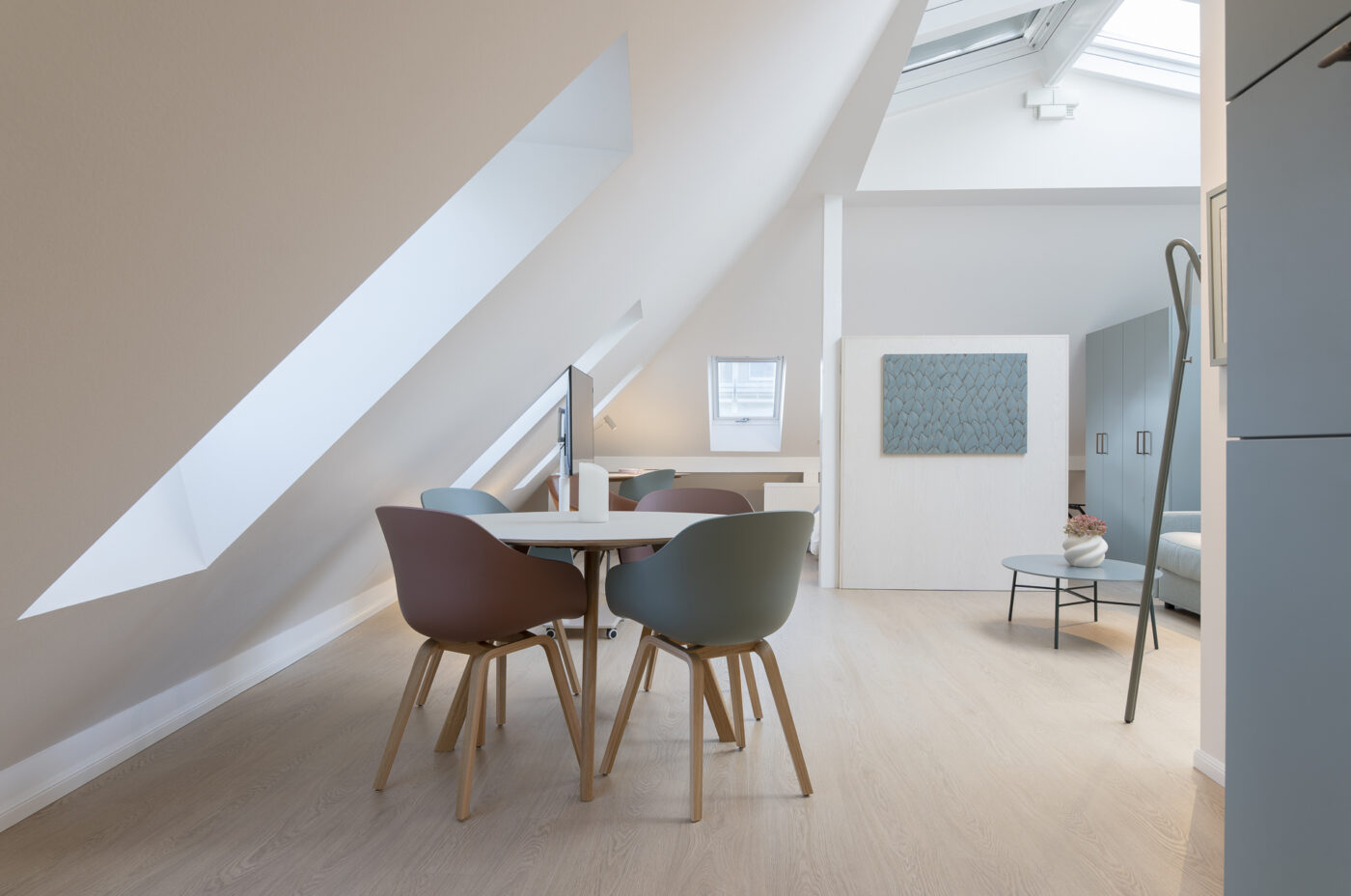 Keyinn Serviced Residences Belair attic apartment with sloped ceilings, skylights, and a minimalist dining set. The space includes pastel chairs, a small table, and bright, natural lighting.