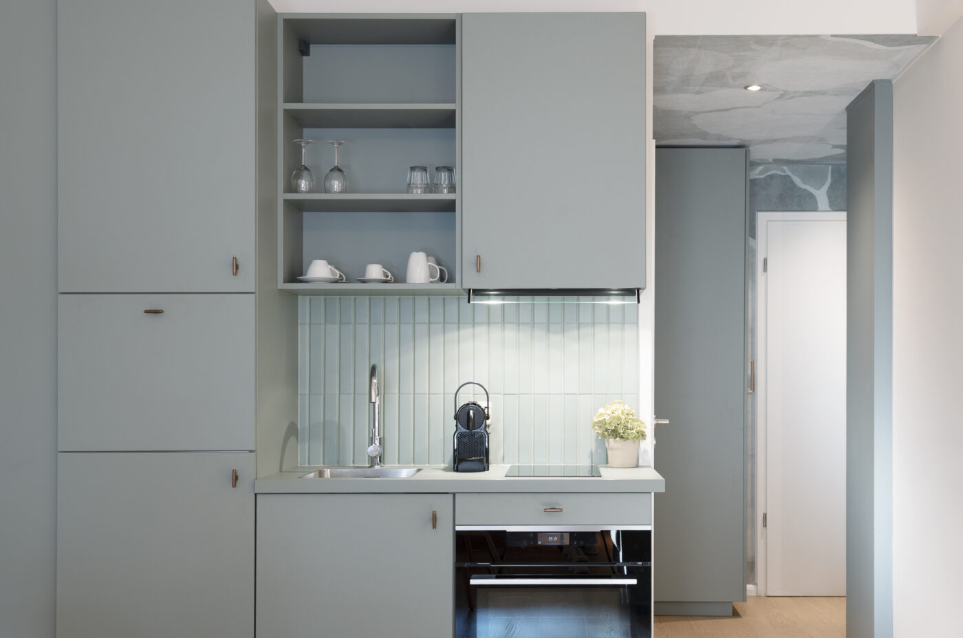 Keyinn Serviced Residences Belair kitchen with blue cabinets, sink, and espresso machine. The space includes a plant, open shelving, and glassware.