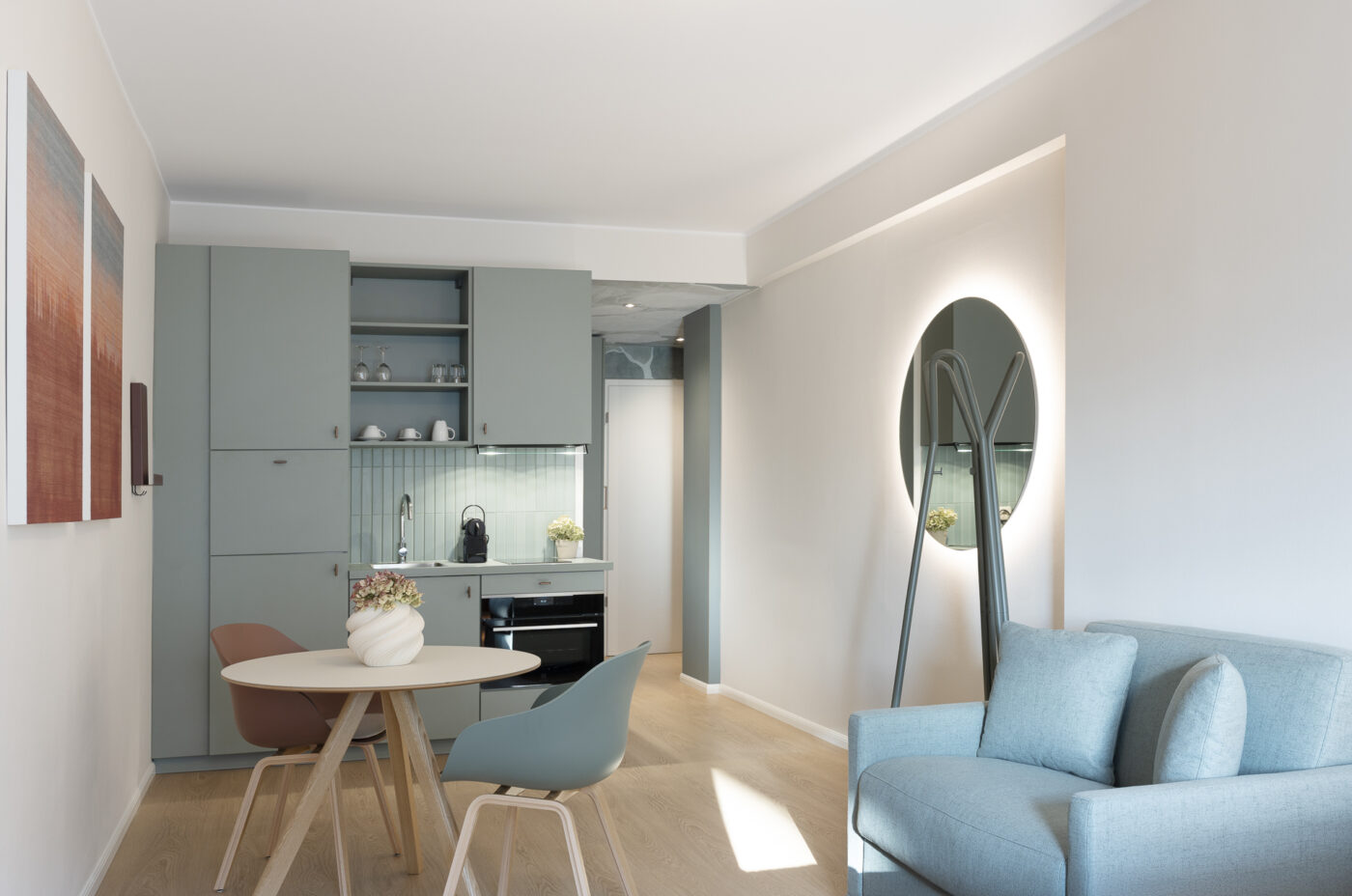 Keyinn Serviced Residences Belair living area with blue cabinets, a table, and chairs. The space includes a sofa, wall mirror, and wall art.