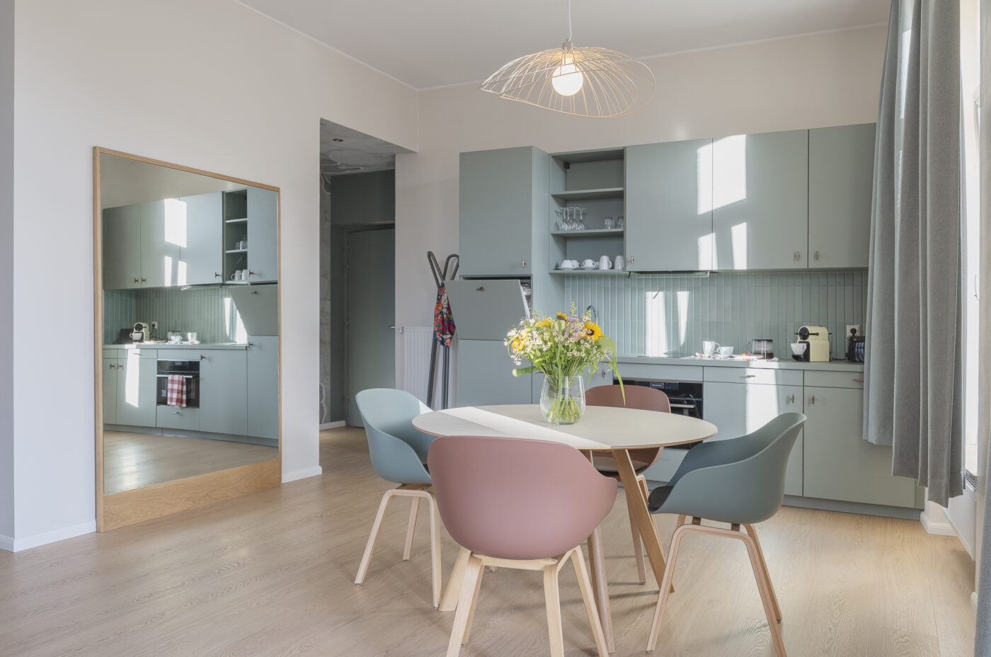 Keyinn Serviced Residences Belair kitchen with pastel green cabinets, wood floors, and a round dining table. The space includes colorful chairs and a floral centrepiece.