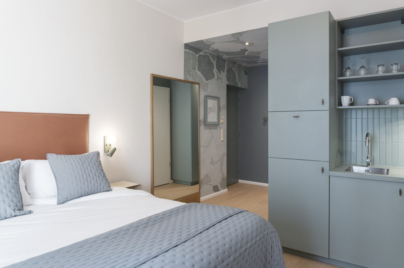 Keyinn Serviced Residences Belair studio with a bed, headboard, and pillows. The space includes a kitchenette, cabinets, and shelving.