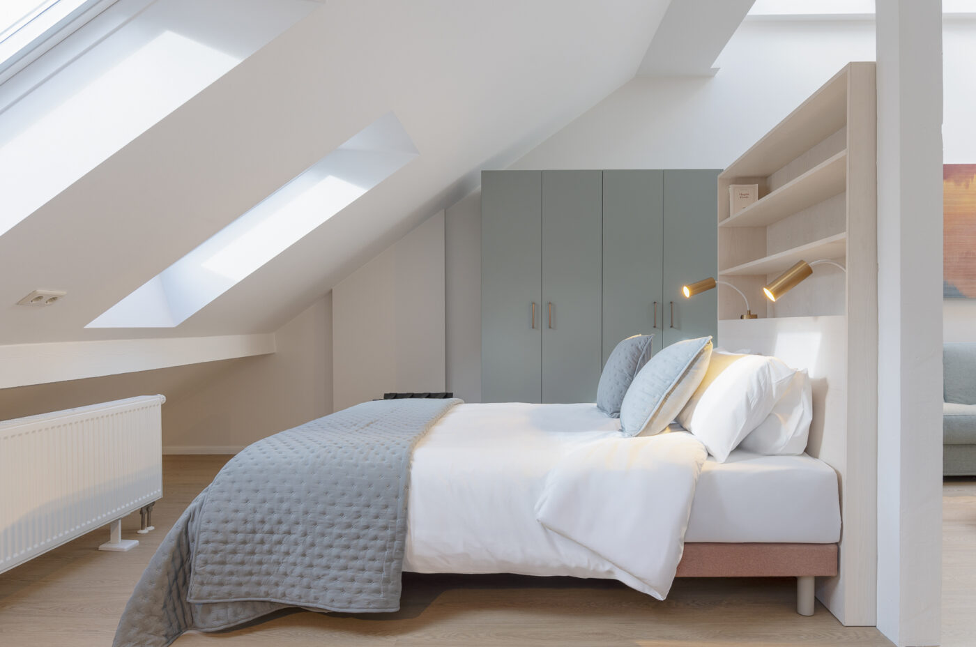 Keyinn Serviced Residences Belair attic bedroom with a skylight, white and grey bedding, and modern sconces. The space includes a minimalist wardrobe and a bright, serene design.