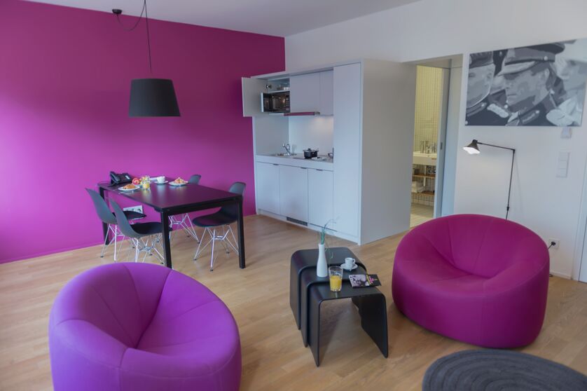 Keyinn Serviced Residences Parc de Merl space with a pink wall, black dining set, and sleek kitchen. 