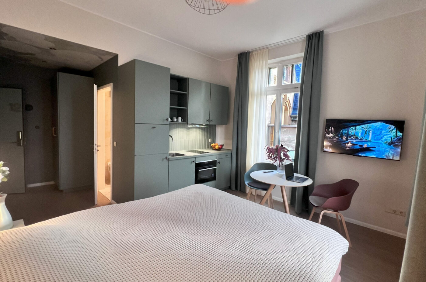 Keyinn Serviced Residences Belair studio with a kitchenette, table, chairs, and TV. The space includes a bed, hallway, and lighting.