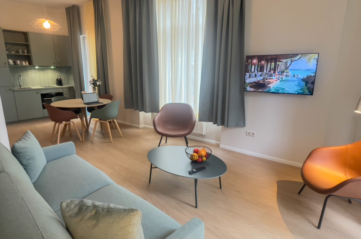 Keyinn Serviced Residences Belair living room with light wood floors and a blue sofa. The space features a round coffee table with a fruit bowl, a TV, and an integrated kitchenette.