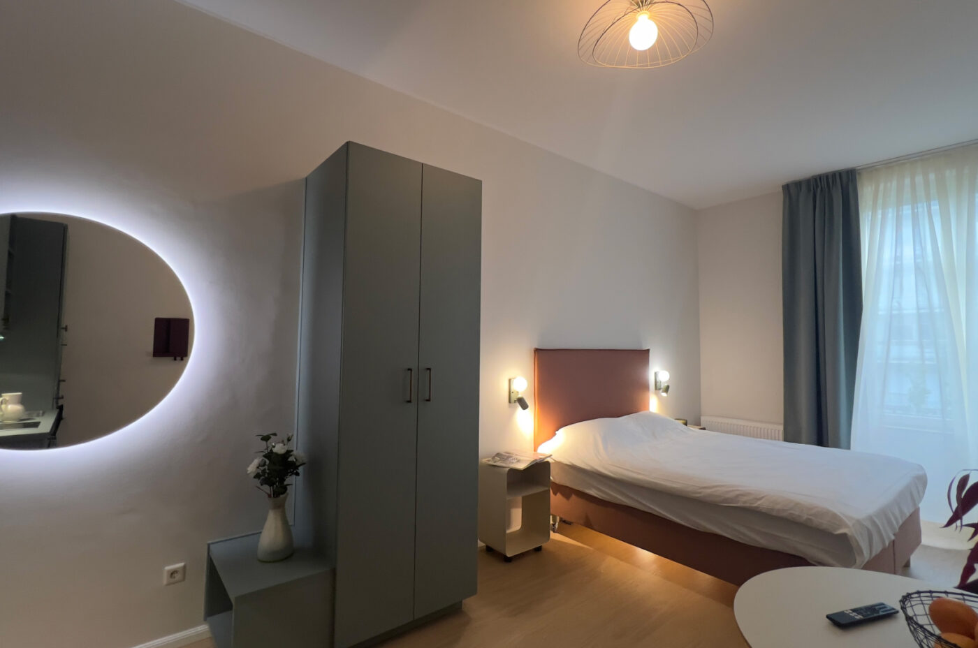 Keyinn Serviced Residences Belair bedroom with a bed, cabinet, and mirror. The space includes a vase, window, and curtains.