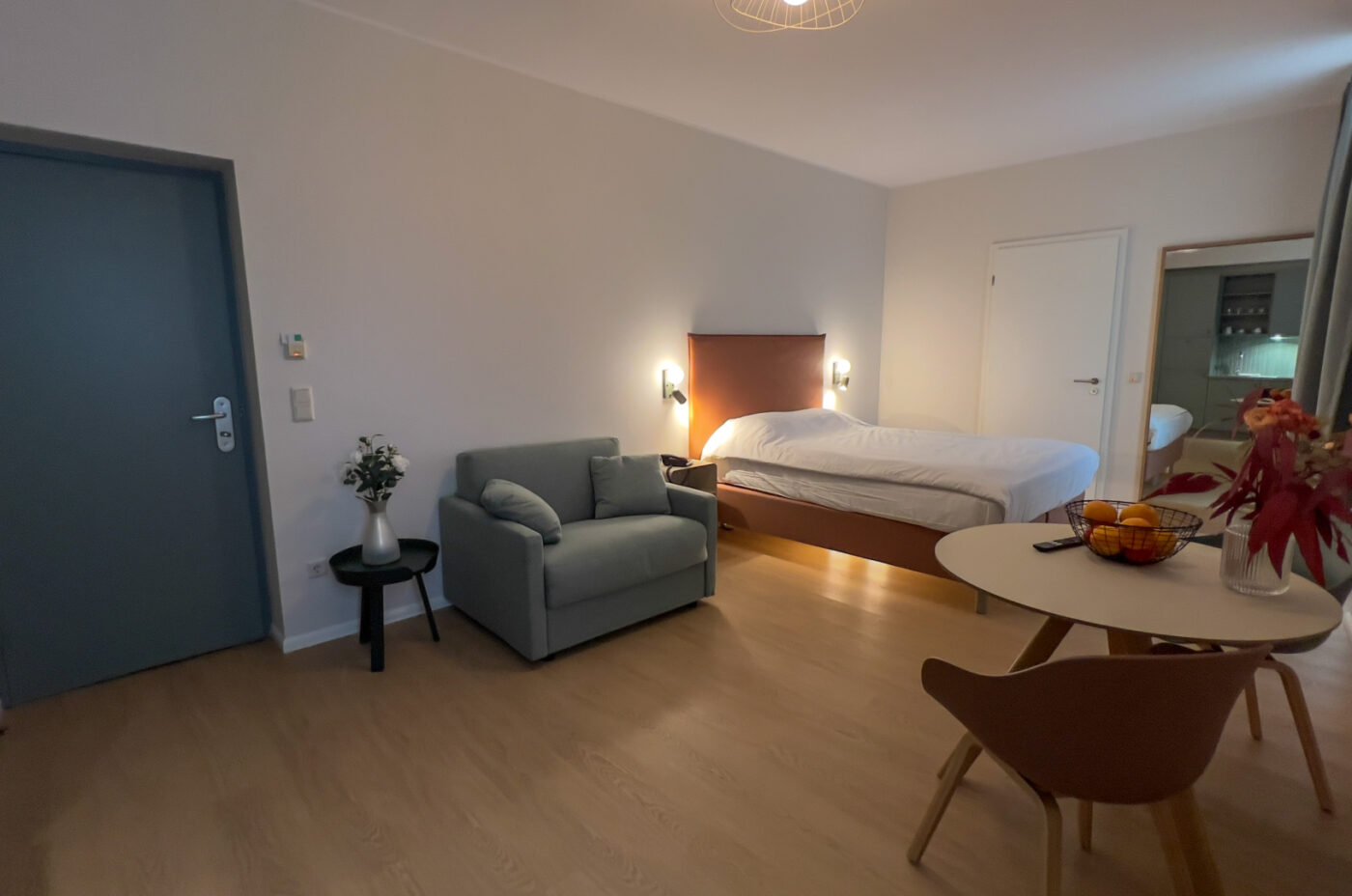 Keyinn Serviced Residences Belair room with a bed, wall lights, sofa, and dining set. The space includes a table, chairs, flowers, and integrated lighting.