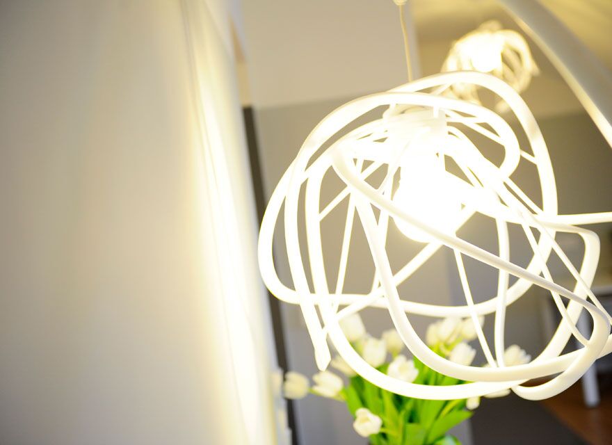Close-up of a modern, abstract light fixture from a Limpertsberg apartment of Keyinn Serviced Residences. with white curves encasing a bulb, casting a soft glow. Tulips in the background add a fresh touch.