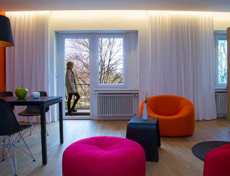 Keyinn Serviced Residence in Parc de Merl featuring red and orange chairs and a balcony with a person overlooking trees.