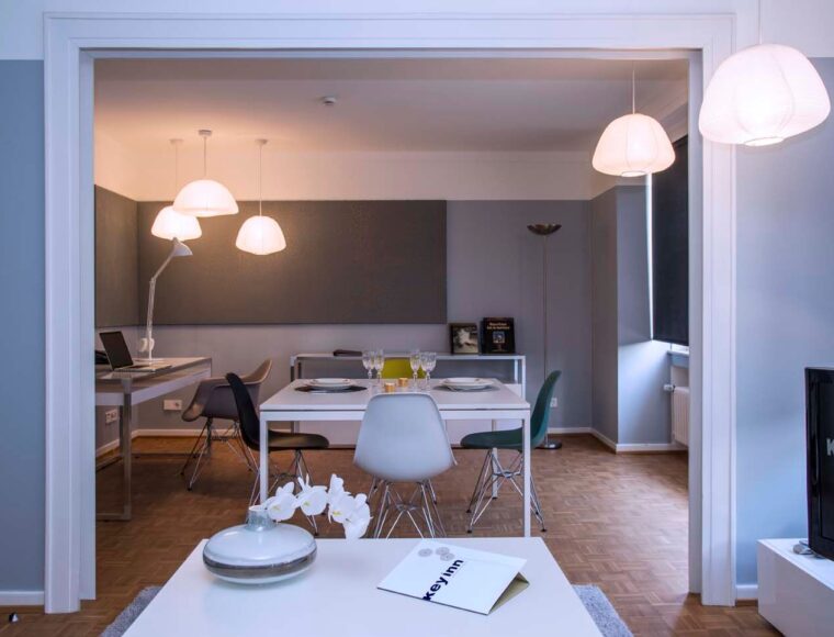 A modern dining & living area at Keyinn Serviced Residences features a dining table set for four, contemporary chairs, stylish pendant lights, & a TV.